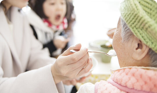 スタッフが入居者に食事の介助をしている様子。食卓での日常の介護シーン。